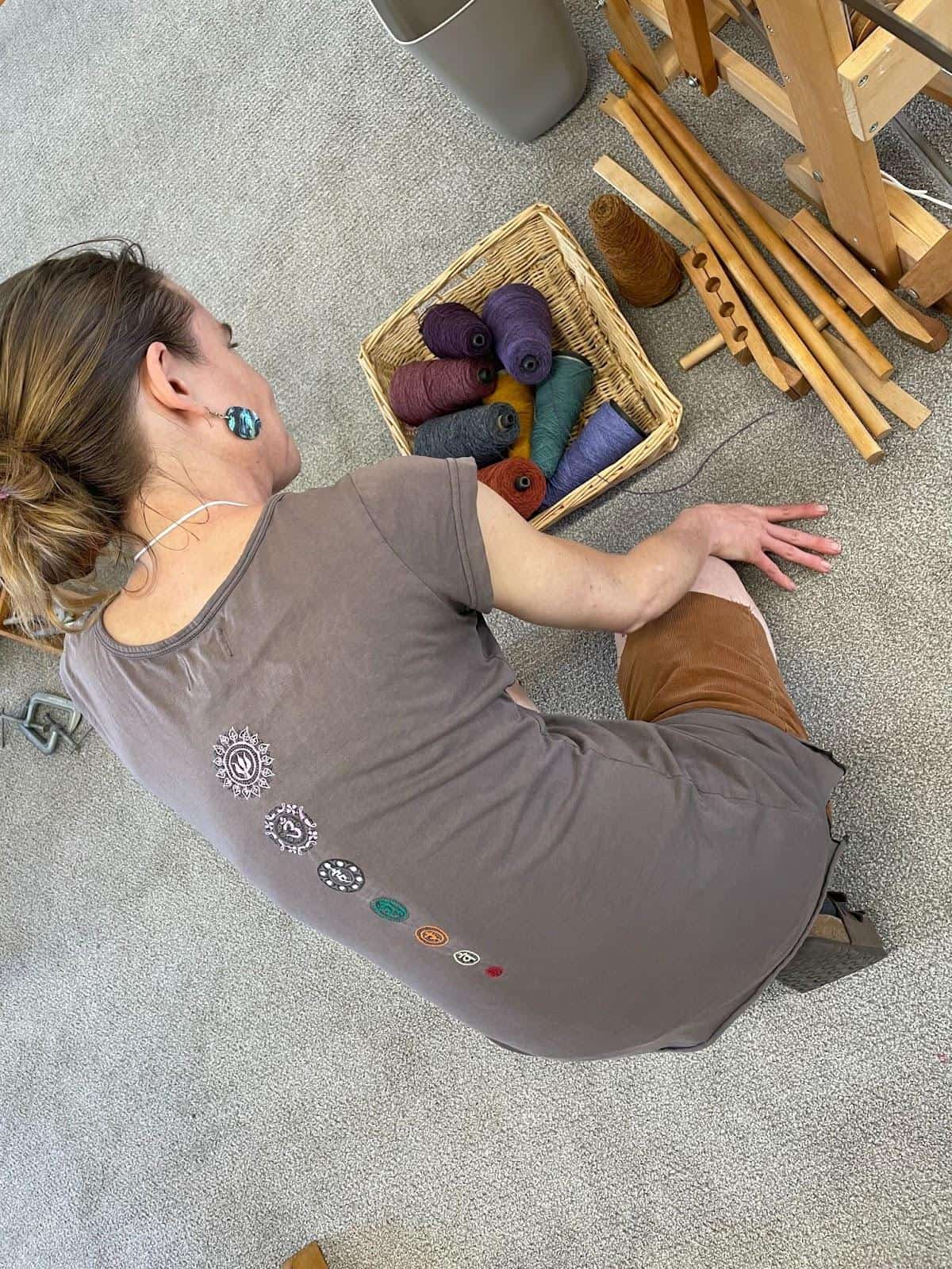 a woman sitting on the floor next to a basket of yarn.